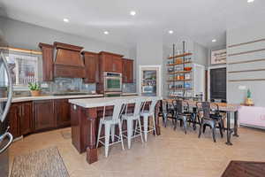 Kitchen with light tile patterned floors, open shelves, light countertops, custom range hood, and backsplash