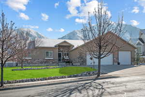 Ranch-style home with a garage, stone siding, a mountain view, a front lawn, and stucco siding