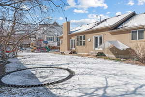 Snow covered house featuring entry steps, a chimney, french doors, a playground, and stucco siding