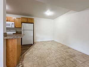 Kitchen featuring a textured ceiling, white appliances, baseboards, brown cabinetry, and stone finish floor