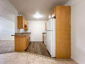 Kitchen with visible vents, a sink, a textured ceiling, white appliances, and baseboards
