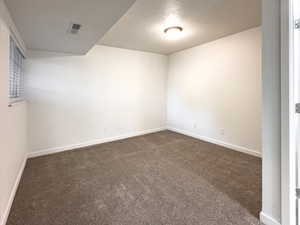 Empty room featuring baseboards, visible vents, dark carpet, and a textured ceiling