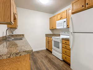 Kitchen with a textured ceiling, white appliances, a sink, baseboards, and dark wood finished floors
