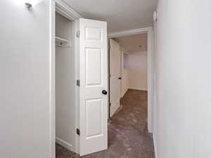 Hall featuring dark carpet, a textured ceiling, and baseboards