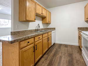 Kitchen with a textured ceiling, white appliances, a sink, baseboards, and dark wood finished floors