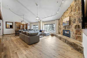 Living room with light wood finished floors, a fireplace, high vaulted ceiling, and track lighting