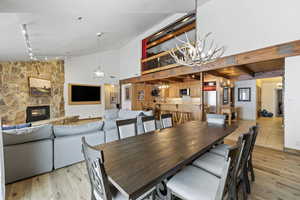 Dining area featuring light wood-style floors, a stone fireplace, high vaulted ceiling, and an inviting chandelier