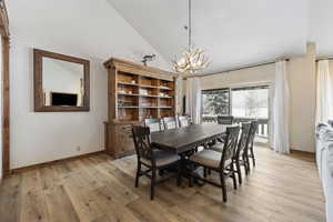 Dining area with high vaulted ceiling, light wood-style flooring, baseboards, and an inviting chandelier