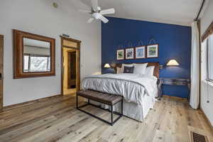 Bedroom featuring lofted ceiling, light wood finished floors, visible vents, and baseboards