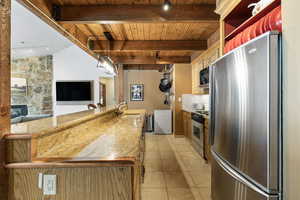 Kitchen with light tile patterned floors, stainless steel appliances, a sink, wood ceiling, and beam ceiling