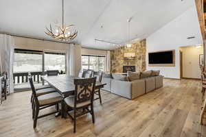 Dining area featuring a notable chandelier, visible vents, a stone fireplace, high vaulted ceiling, and light wood-type flooring