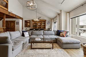 Living room featuring rail lighting, a chandelier, vaulted ceiling, and wood finished floors