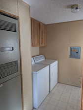 Laundry room with wallpapered walls, electric panel, washing machine and clothes dryer, a textured ceiling, and light floors