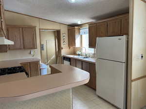 Kitchen with light floors, lofted ceiling, freestanding refrigerator, a sink, and wallpapered walls