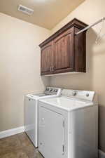 Washroom with visible vents, washer and clothes dryer, cabinet space, light tile patterned floors, and baseboards