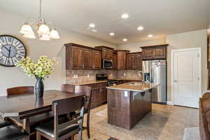 Kitchen featuring dark brown cabinets, an island with sink, decorative backsplash, appliances with stainless steel finishes, and a sink