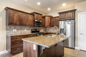 Kitchen featuring a sink, light stone countertops, tasteful backsplash, and stainless steel appliances