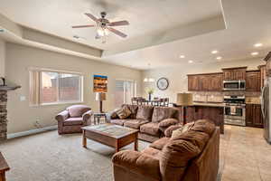 Living room featuring light tile patterned floors, a ceiling fan, baseboards, a tray ceiling, and recessed lighting