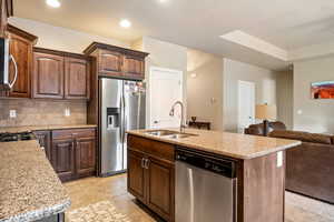 Kitchen featuring a sink, backsplash, light stone countertops, stainless steel appliances, and a kitchen island with sink