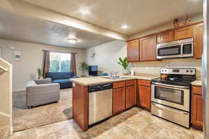 Kitchen with stainless steel appliances, a peninsula, a sink, open floor plan, and light countertops