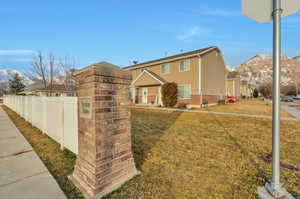 View of front of house with a mountain view, brick siding, fence, a residential view, and a front lawn