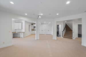 Unfurnished living room with light carpet, stairway, and recessed lighting