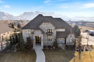 French country inspired facade with stone siding, a shingled roof, a mountain view, and a front yard