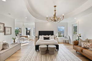 Primary bedroom with a raised ceiling, multiple windows, light wood-style flooring, and an inviting chandelier