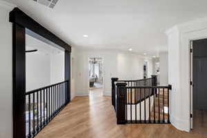 Hall featuring crown molding, light wood-style flooring, an upstairs landing, a chandelier, and baseboards