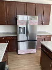 Kitchen with light wood-style floors, dark brown cabinetry, light countertops, and stainless steel refrigerator with ice dispenser