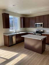 Kitchen featuring a kitchen island, light countertops, appliances with stainless steel finishes, light wood-style floors, and a sink