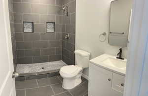 Full bath with toilet, tile patterned floors, tiled shower, and vanity