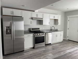 Kitchen featuring white cabinets, a sink, appliances with stainless steel finishes, under cabinet range hood, and stone countertops