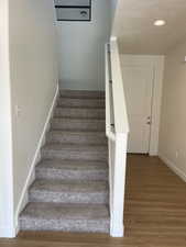 Stairway featuring recessed lighting, a textured ceiling, baseboards, and wood finished floors