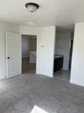 Unfurnished bedroom featuring light colored carpet, a textured ceiling, ensuite bathroom, and baseboards
