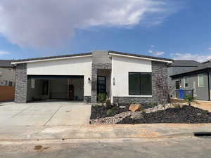 Contemporary home with stone siding, stucco siding, an attached garage, and concrete driveway