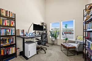 Carpeted office with baseboards and a towering ceiling