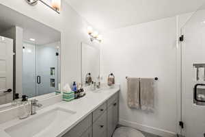 Full bath featuring a sink, baseboards, a stall shower, and double vanity