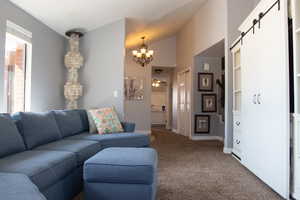 Carpeted living area with a barn door, lofted ceiling, baseboards, and an inviting chandelier