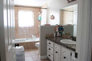 Bathroom featuring tiled shower / bath combo, toilet, vanity, and tile patterned flooring