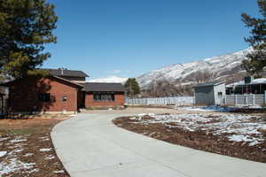 View of snow covered exterior with a storage unit, a mountain view, brick siding, and fence