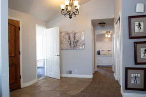 Corridor featuring stone tile flooring, baseboards, an inviting chandelier, and lofted ceiling