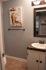 Half bath featuring vanity, toilet, baseboards, and tile patterned flooring