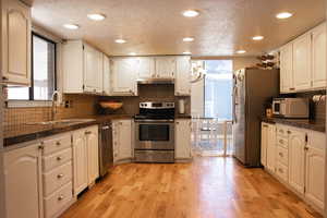 Kitchen featuring a sink, under cabinet range hood, granite countertops, stainless steel appliances, and light wood-style floors