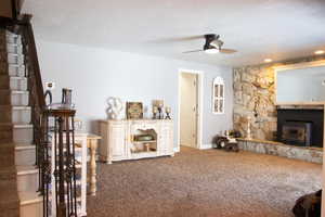 Carpeted family room located directly off of kitchen featuring a textured ceiling, a fireplace, baseboards, ceiling fan, and stairs