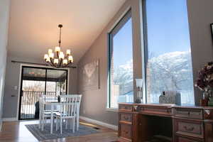 Dining area with visible vents, baseboards, lofted ceiling, wood finished floors, and a notable chandelier. Large windows capture the picturesque mountains just East of the home.