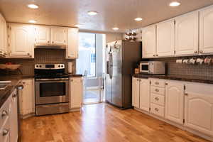 Kitchen with stainless steel appliances, light wood-style floors, under cabinet range hood, white cabinetry, granite countertops, and backsplash