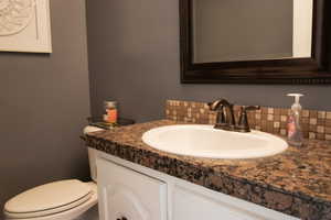 half Bathroom with backsplash, vanity, and toilet