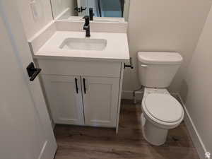 Half bathroom featuring baseboards, toilet, wood finished floors, and vanity