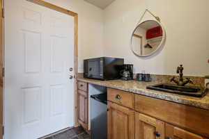 Kitchen featuring brown cabinetry, light stone counters, refrigerator, black microwave, and a sink